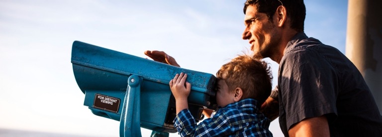 Vader ondersteunt zijn zoon die door een grote verrekijker kijkt