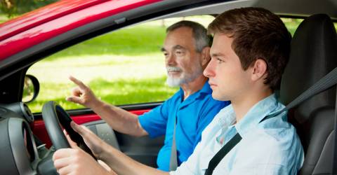 Jonge jongen achte het stuur in de auto met een oudere man ernaast 