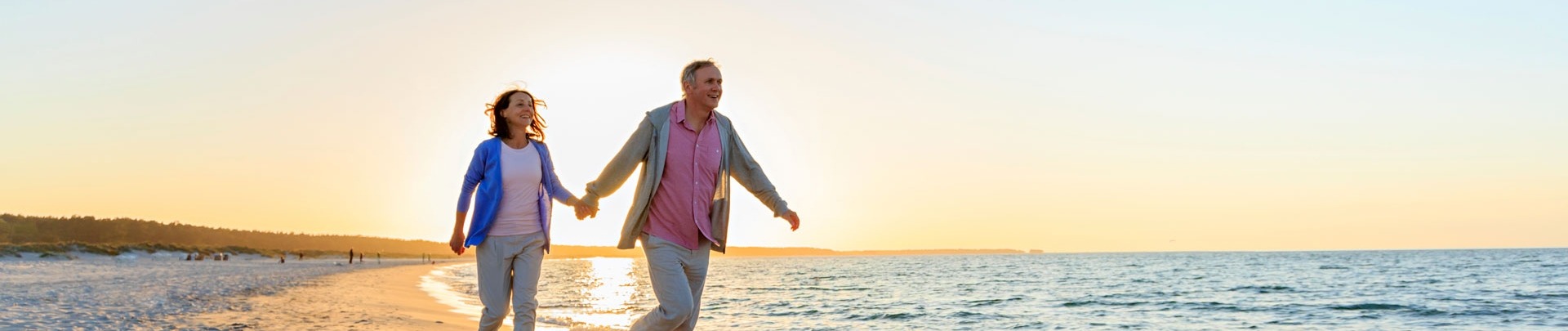 een oudere man en vrouw die over het strand rennen met de zon achter zich